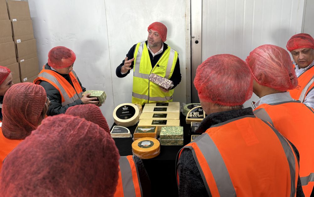 A man showing a variety of cheeses to people.